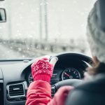 Woman in the red jacket, hat and christmas gloves is driving on the highway at the winter snowfall.  View from the back seat of the car. concept.