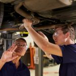 Mechanic And Male Trainee Working Underneath Car Together